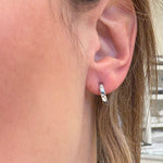 Close-up of an ear wearing a white gold small hoop earring with a blurred background