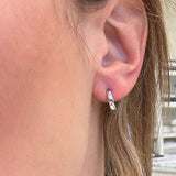 Close-up of an ear wearing a white gold small hoop earring with a blurred background