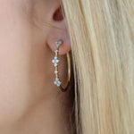 A close-up of a woman's ear wearing a gold hoop earring adorned with three small floral clusters of clear diamonds.