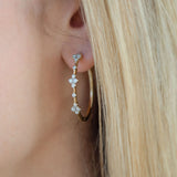 A close-up of a woman's ear wearing a gold hoop earring adorned with three small floral clusters of clear diamonds.