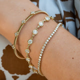Three 14K yellow gold bracelets with clear diamonds worn stacked on a woman's wrist. The bracelets include a textured bangle, a chain with round diamonds, and a tennis-style link bracelet.