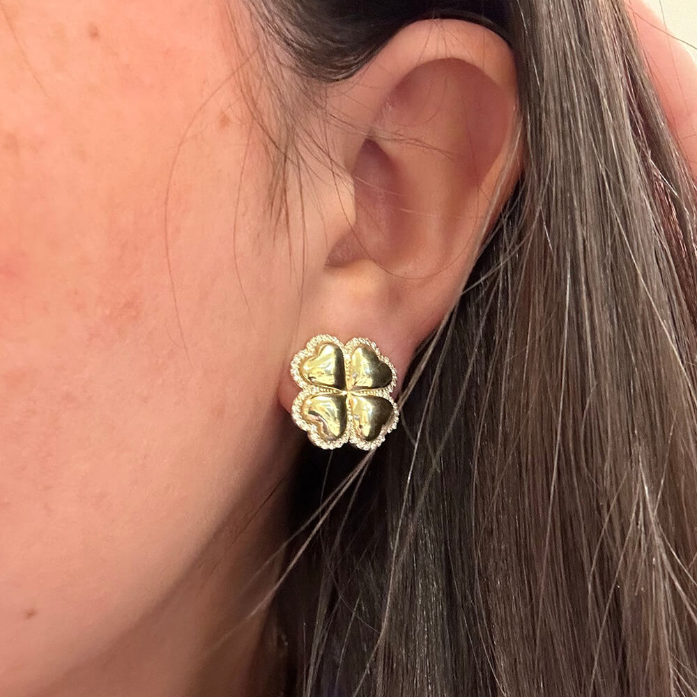 A close-up of a woman's ear wearing a 14K gold four-leaf clover stud earring.