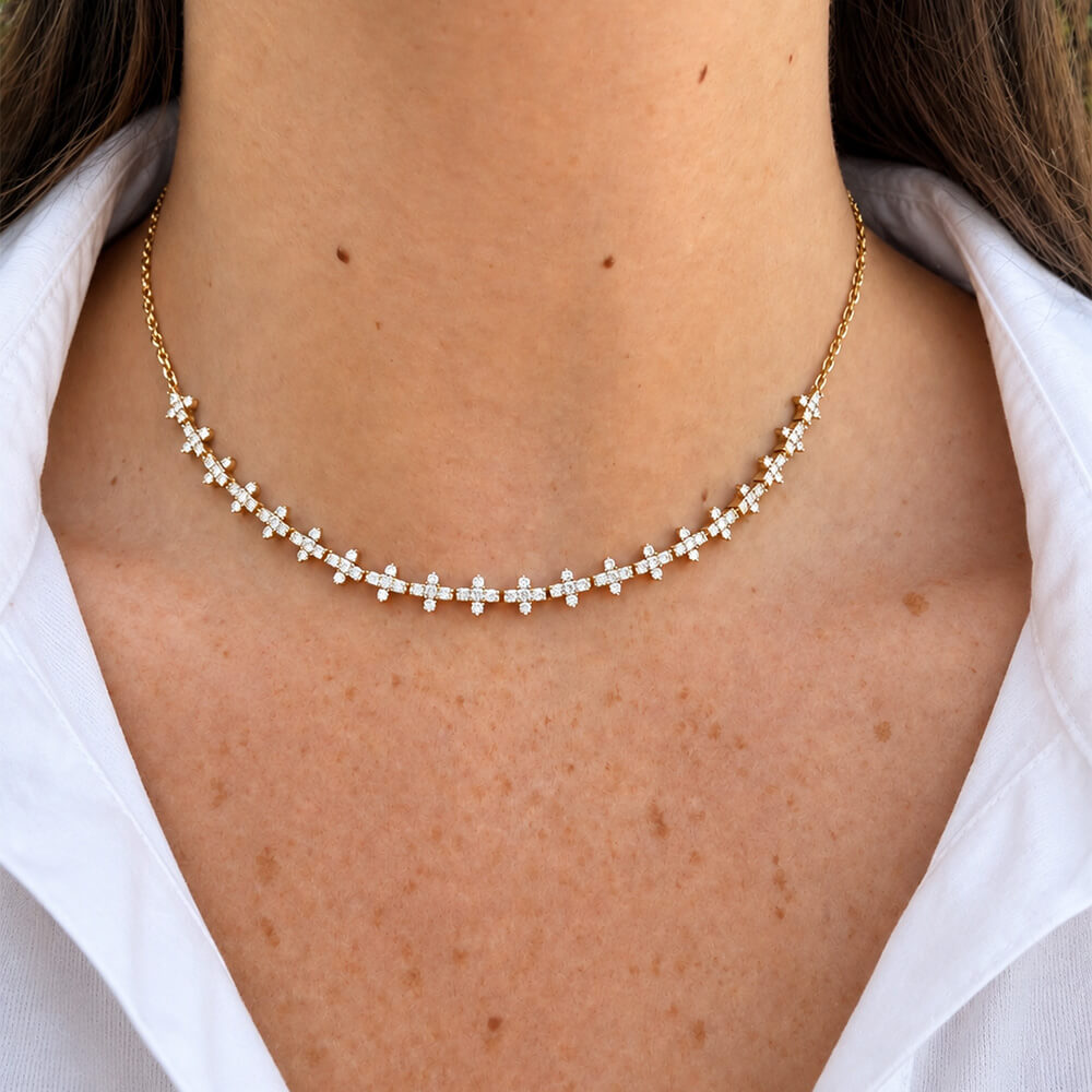 A delicate 14K yellow gold chain necklace featuring a row of small diamond flower-shaped accents, shown worn on a model's neck over a white collared shirt.