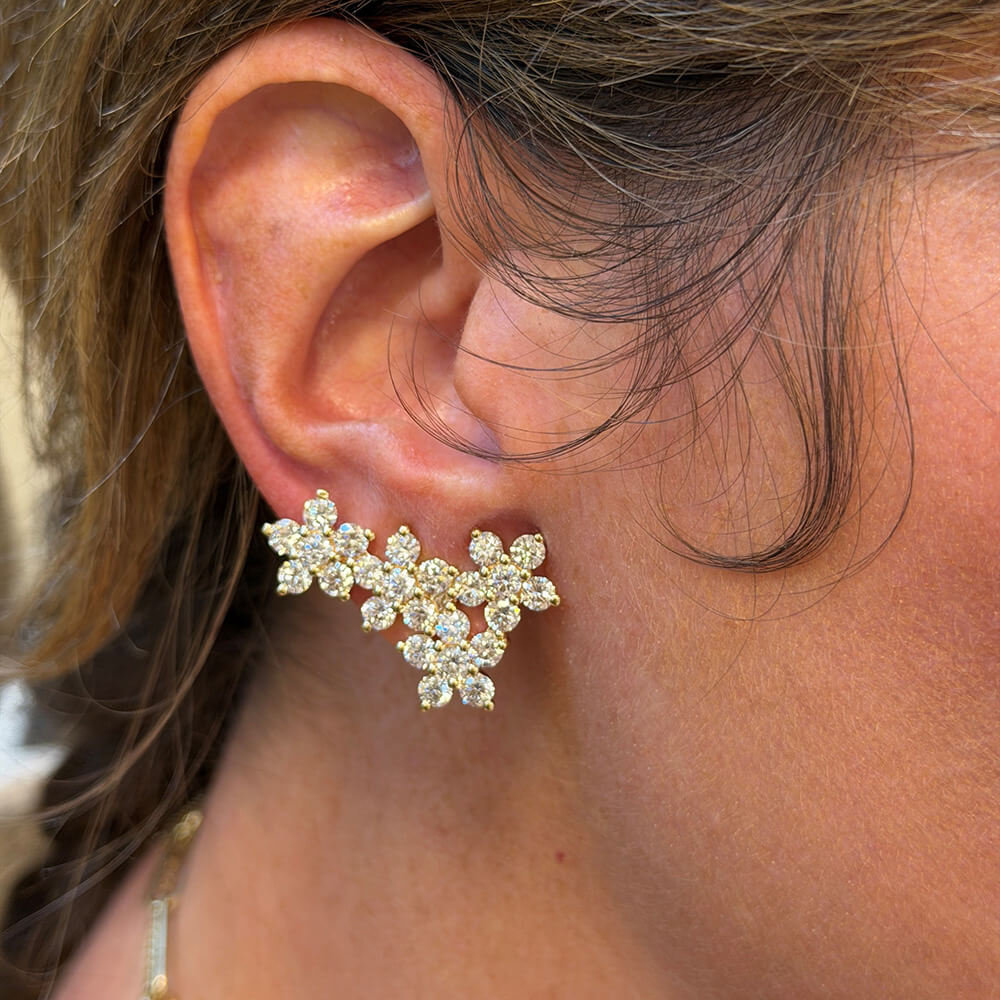 A close-up of a woman's ear wearing a 14K gold floral cluster stud ear climber earring with clear diamonds.