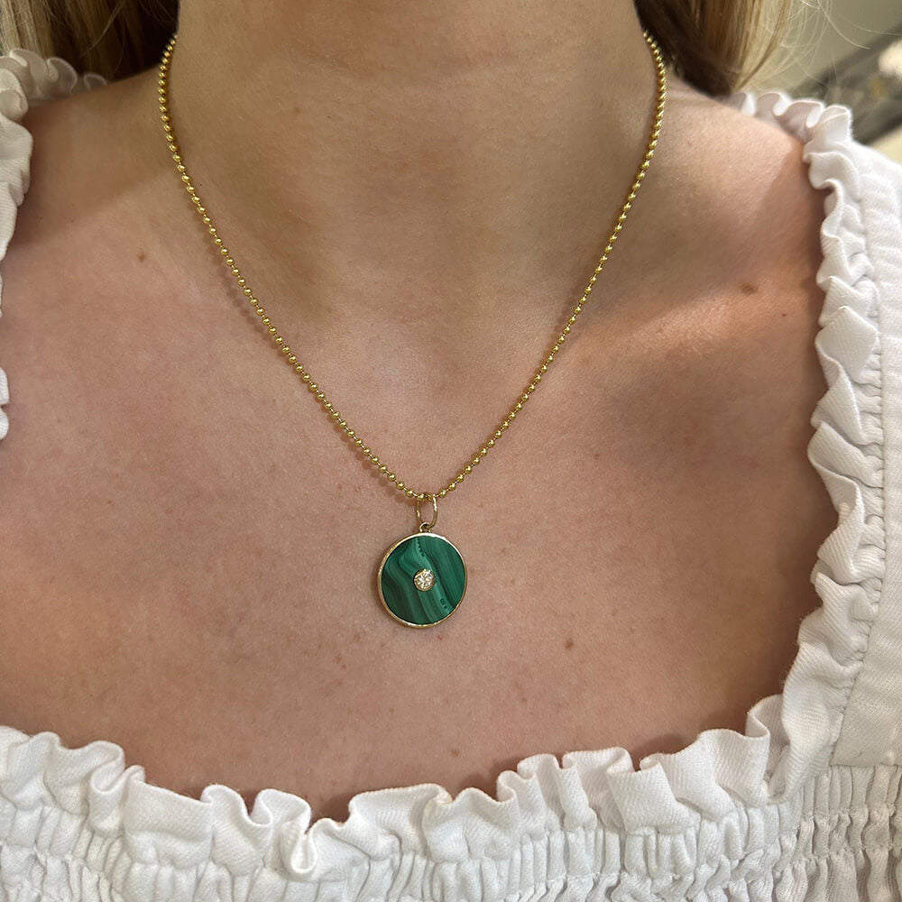 A close-up of a woman wearing a 14K gold chain necklace with a round green malachite pendant featuring a center diamond