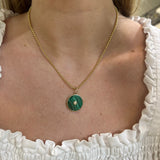 A close-up of a woman wearing a 14K gold chain necklace with a round green malachite pendant featuring a center diamond