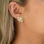 A close-up of a woman's ear wearing a 14K yellow gold leaf-shaped stud earring adorned with small clear pavé diamonds.