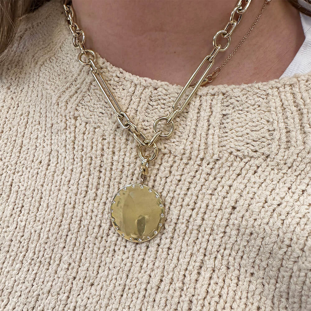 A close-up of a woman wearing a 14K yellow gold chain necklace with a round, 14K yellow gold pendant over a cream-colored knit sweater.