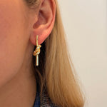 A close-up of a woman's ear wearing a 14K gold tube love knot drop earring 