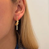A close-up of a woman's ear wearing a 14K gold tube love knot drop earring 