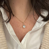 A close-up of a woman wearing a delicate 14K gold chain necklace with a round clear white topaz gemstone pendant, 