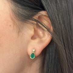 Close-up of an ear wearing a green earring with dark hair in the background