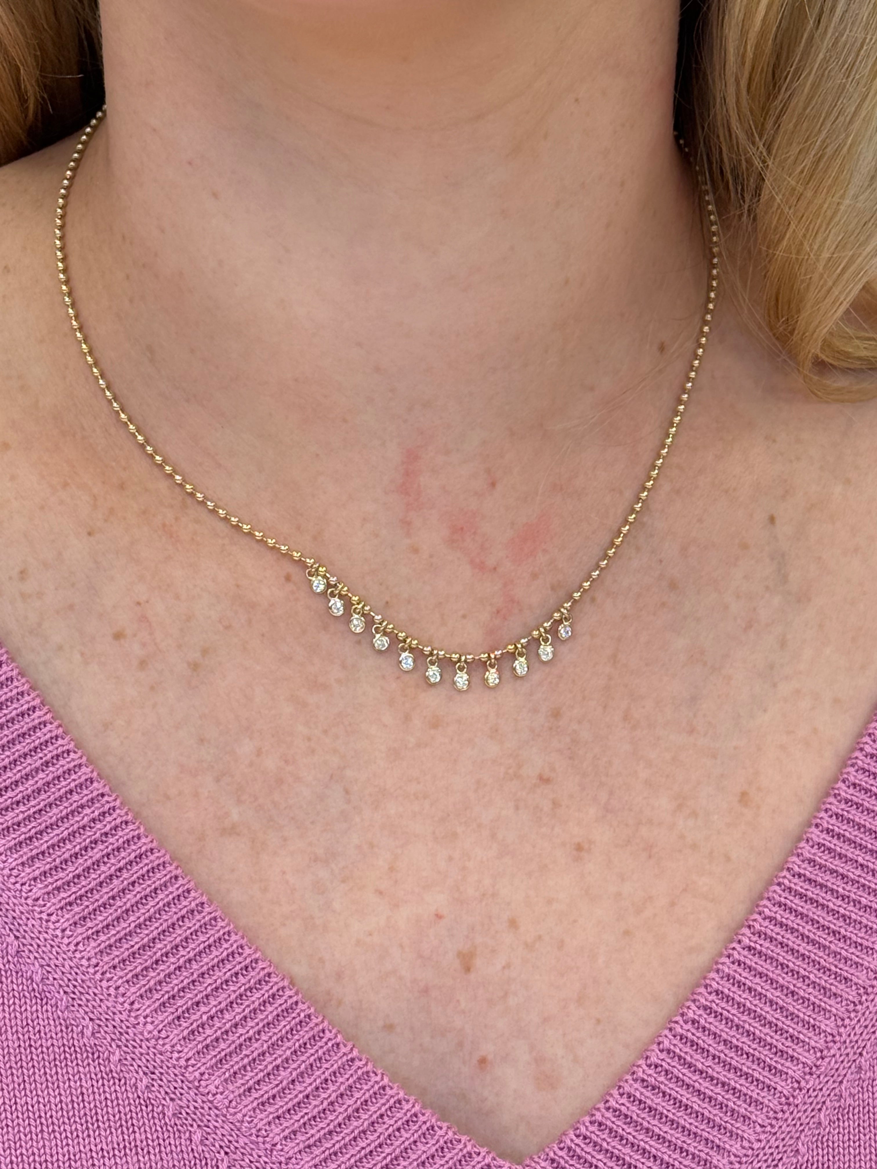 14K Gold necklace with diamonds worn by a woman against a pink sweater background
