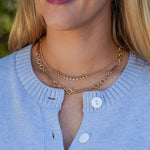 Close-up of a woman wearing a gold necklaces with a blurred natural background