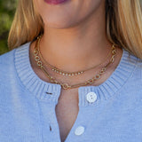 Close-up of a woman wearing a gold necklaces with a blurred natural background