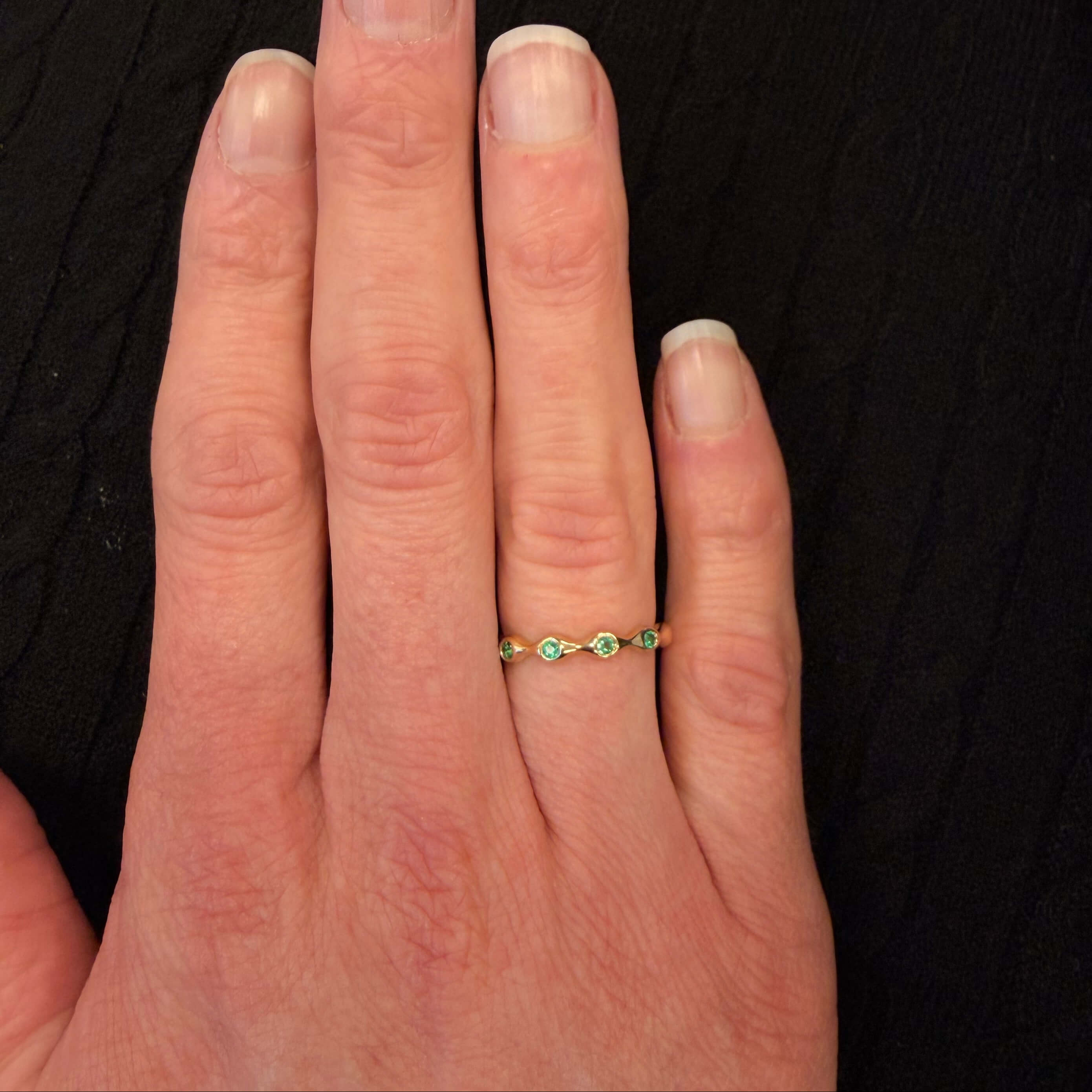 Hand wearing a 14K gold ring with emerald gemstones on a black background