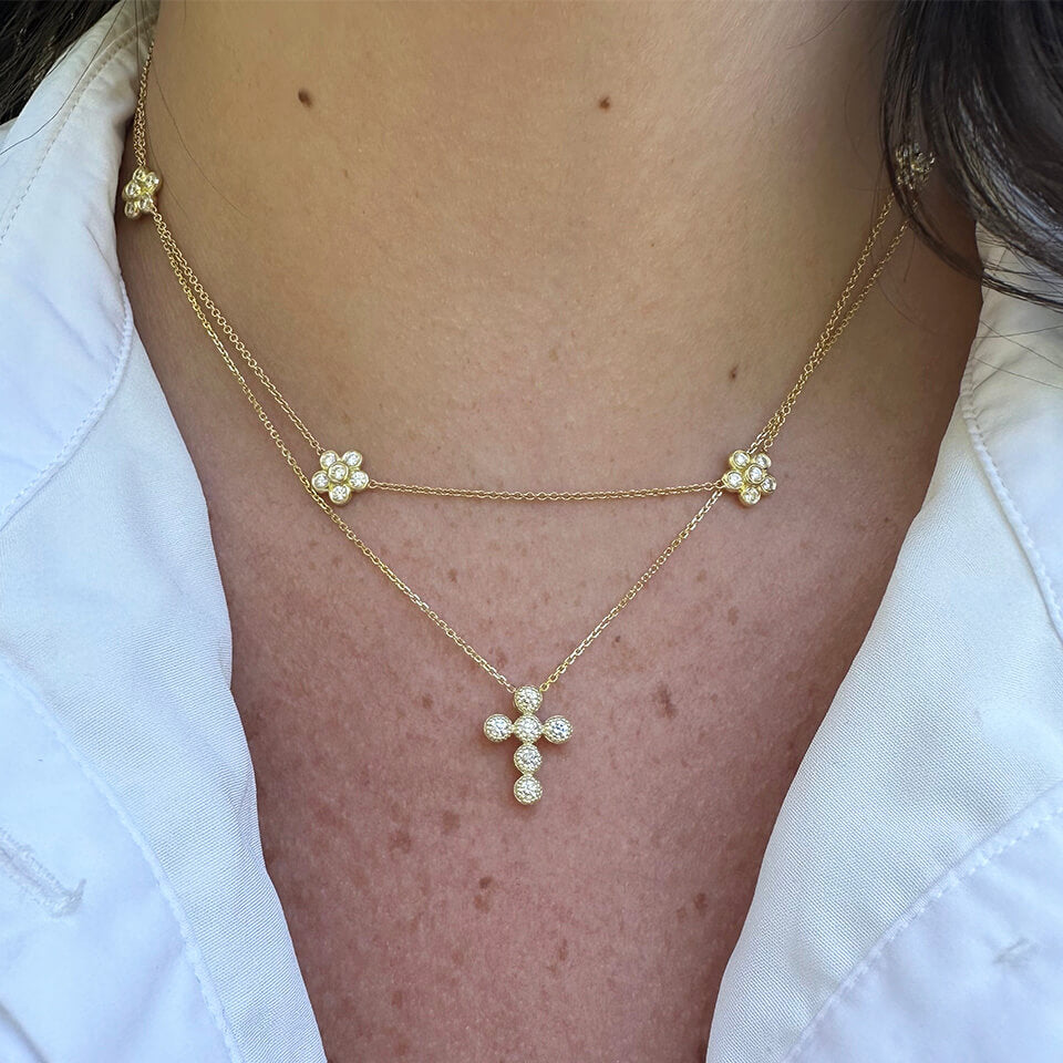 A close-up of a woman wearing a delicate 14K gold diamond cross pendant pendant necklace