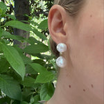 Close-up of a woman wearing pearl earrings with a blurred green outdoor background