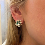 Close-up of a person wearing a floral earring with green stones.