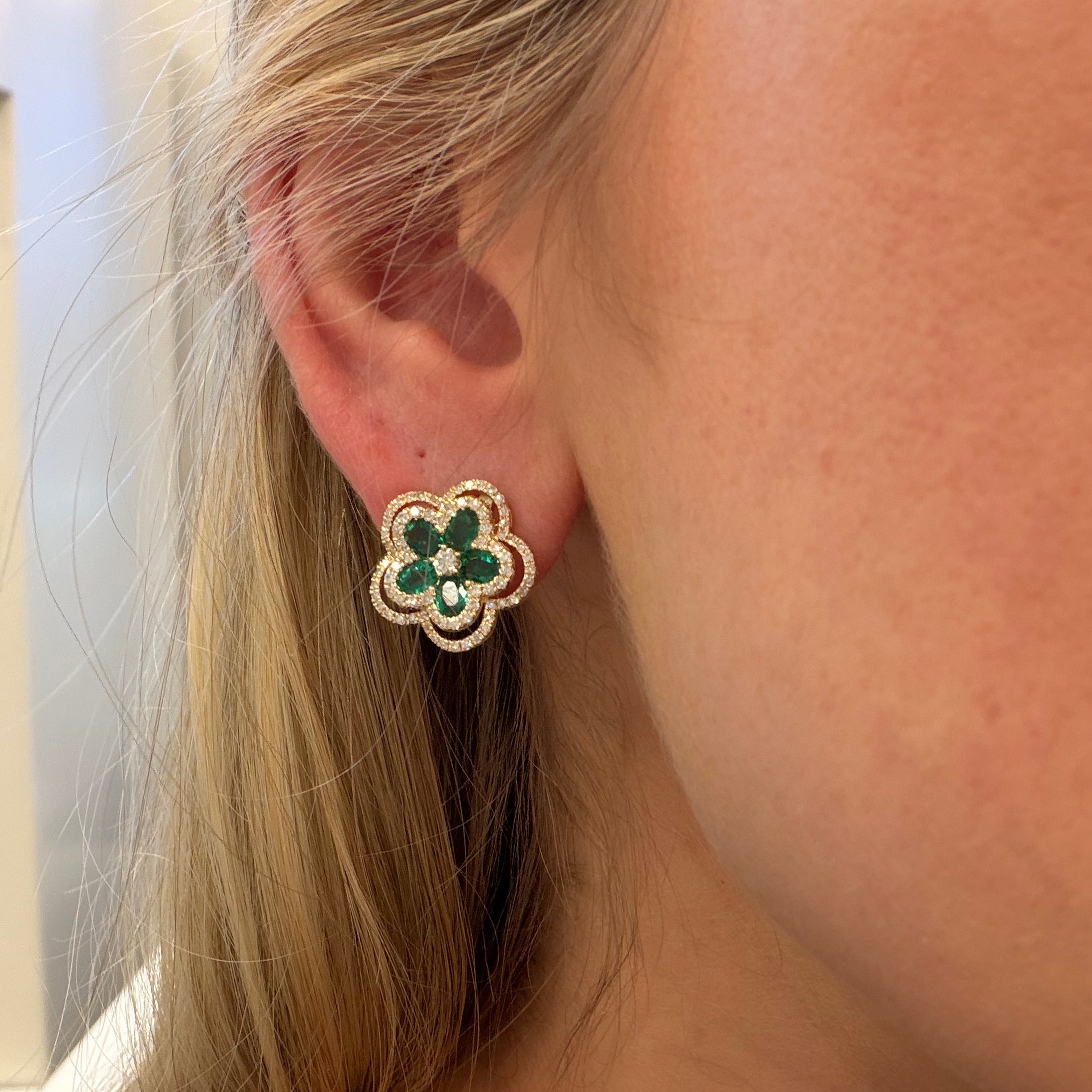 Close-up of a person wearing a floral earring with green stones.