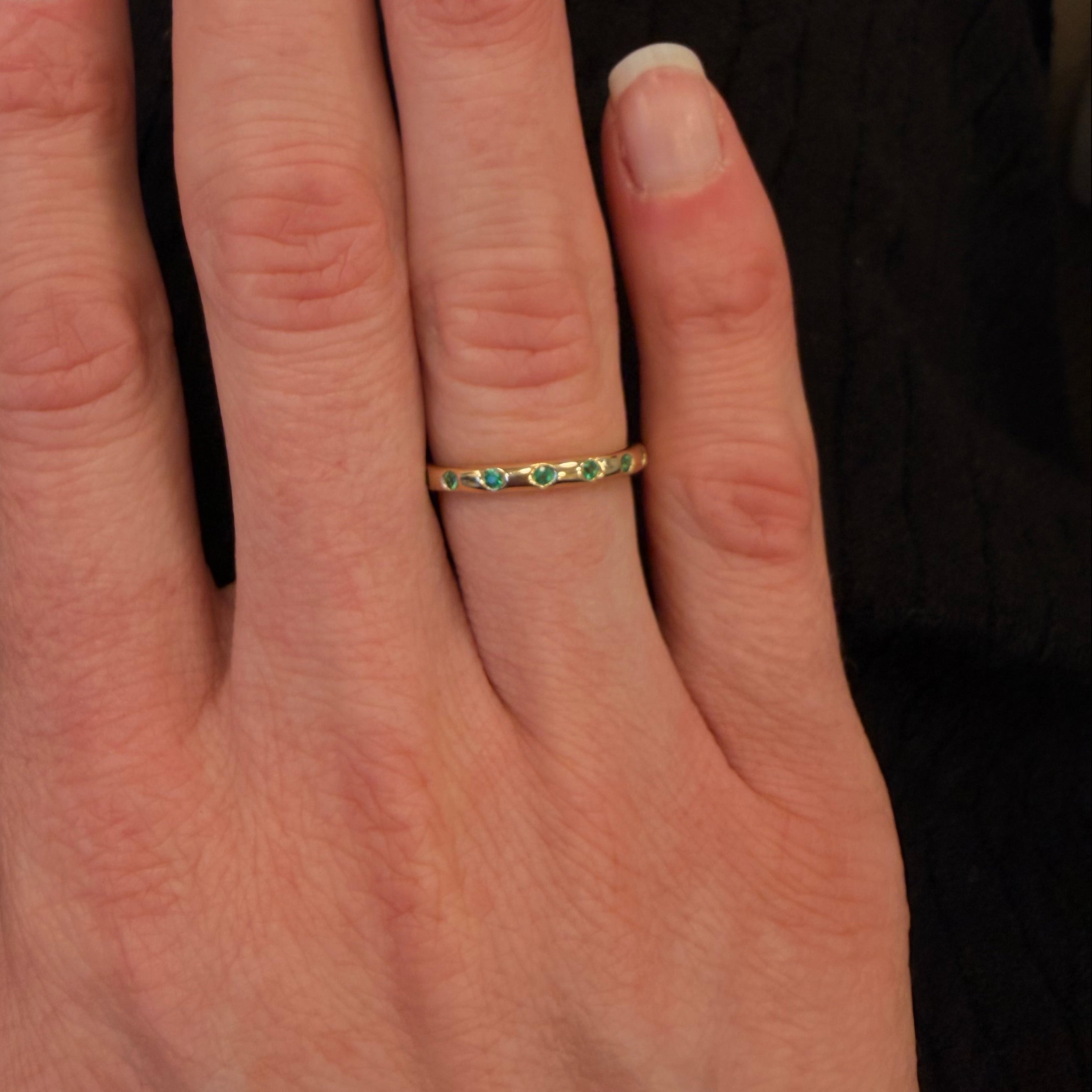 Woman wearing a 14K gold ring with emerald gemstones on a blurred background