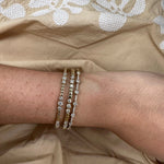 Close-up of a woman's wrist wearing 14K gold and diamond bracelets on a beige fabric background