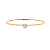 A 14K yellow gold bangle bracelet with a single diamond centerpiece, set on a white background.