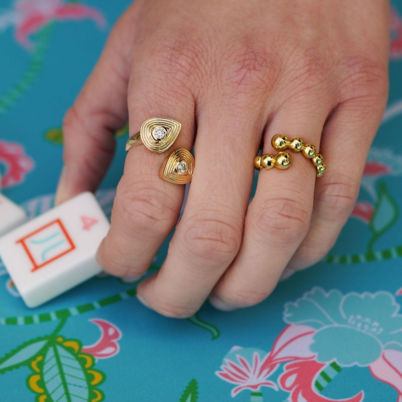 Hand wearing gold rings on a colorful tablecloth with game pieces.