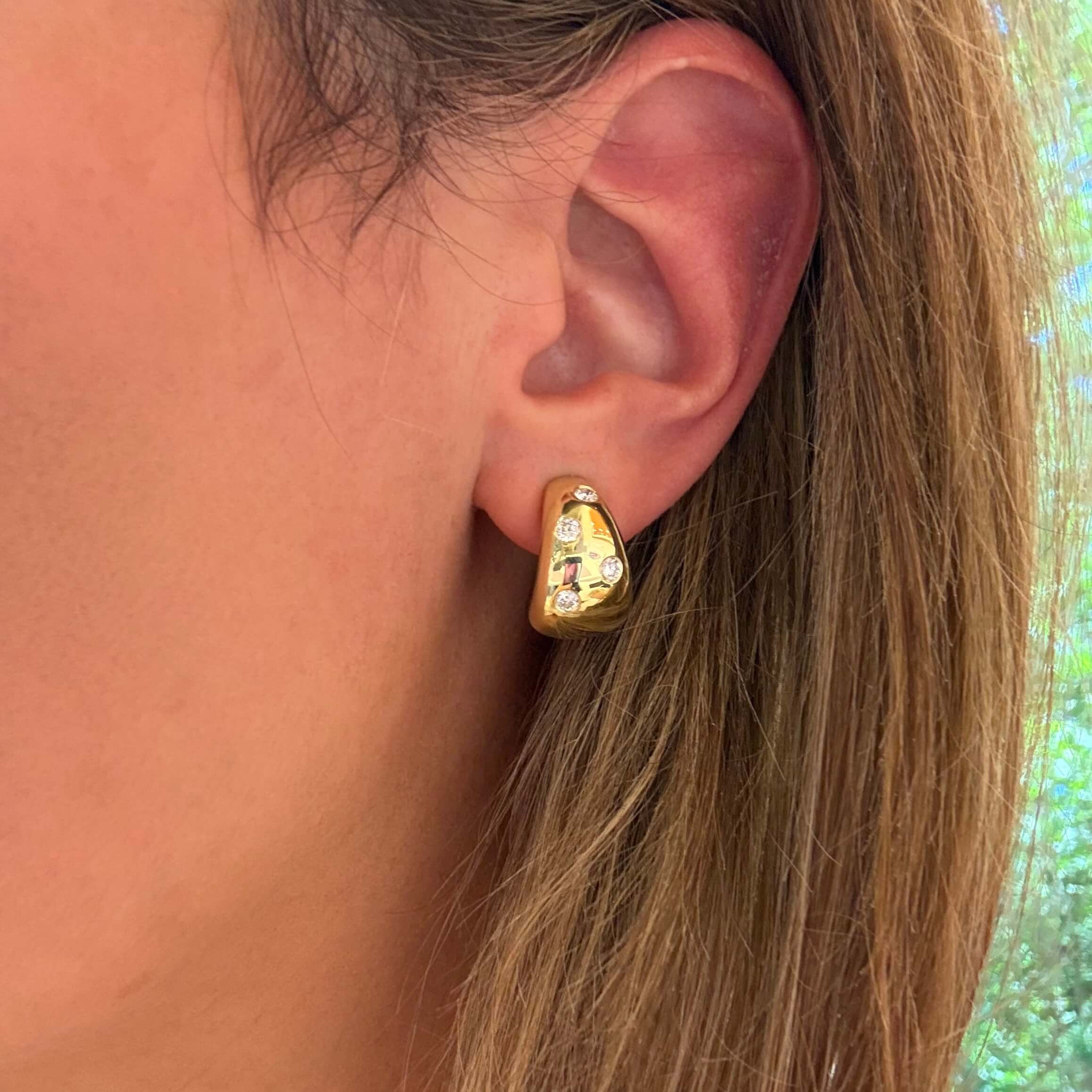 Close-up of a woman wearing a gold huggie earring with embedded diamonds