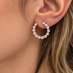 A close-up of a woman's ear wearing a 14k yellow gold open circle earring set with multiple clear round diamonds.