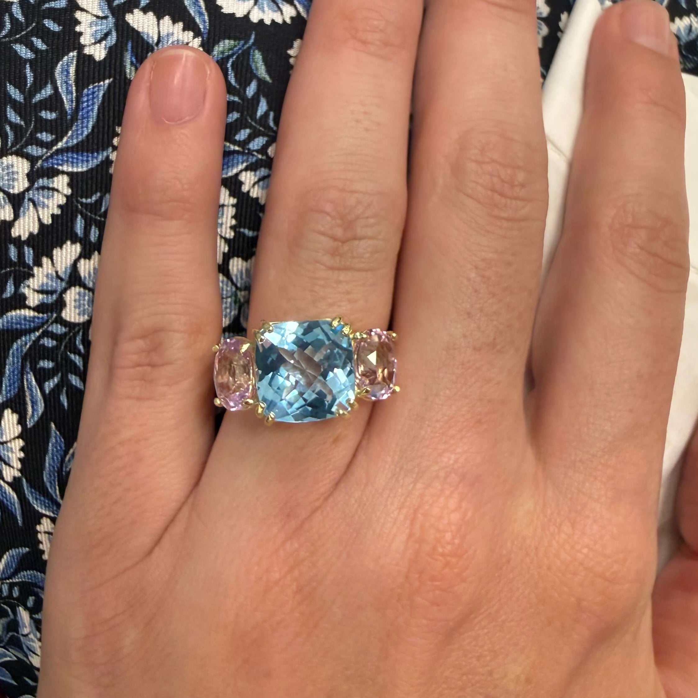 Hand wearing a ring with a blue topaz and pink kunzite on a floral-patterned fabric background