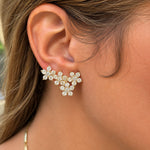 A close-up of a woman's ear wearing a 14k yellow gold cluster climber earring adorned with clear diamonds, set against her skin and brown hair.
