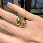 A close-up of a hand wearing a wide, chunky 14K gold ring with two rounded, polished sections, one of which is set with diamonds