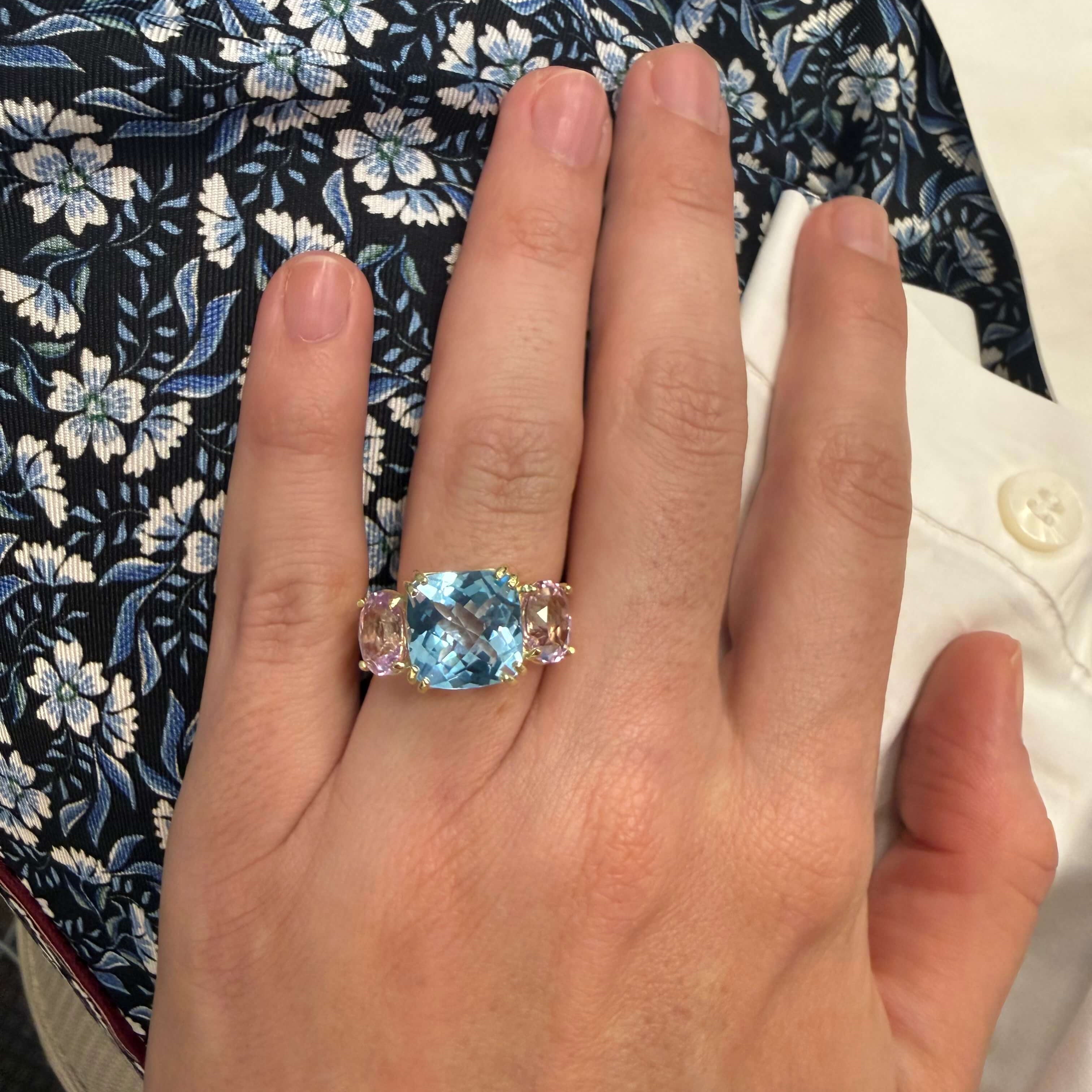 Hand wearing a ring with a blue gemstone on a floral-patterned fabric background