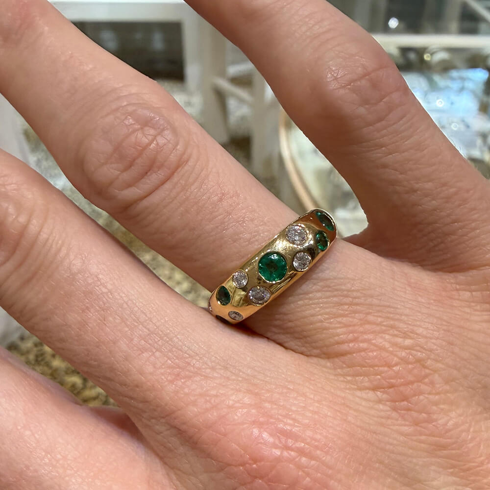 A close-up of a hand wearing a 14K yellow gold ring adorned with emeralds and diamonds