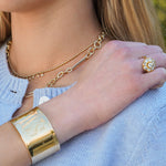 Close-up of a woman wearing gold jewelry including earrings, cuff bracelet, and ring.