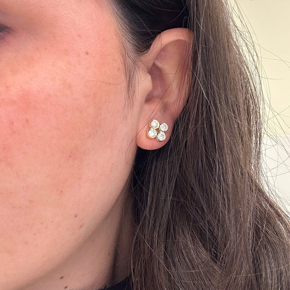 Close-up of an ear wearing a three-stone earring with a neutral background