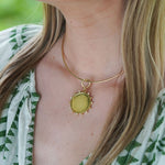 A close-up of a woman wearing a delicate gold necklace with a round 18K gold disc pendant with beads and diamonds