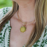 A close-up of a woman wearing a delicate gold necklace with a round 18K gold disc pendant with beads and diamonds