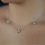 A close-up of a delicate 18k white gold chain necklace worn by a model, featuring three small, flower-like charms embellished with pave diamonds