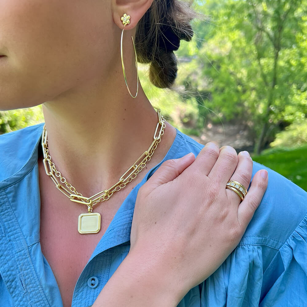 Woman wearing 18K gold jewelry including a necklace, hoop earrings, and rings