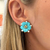 Close-up of a turquoise flower-shaped earring worn by a person with blonde hair.