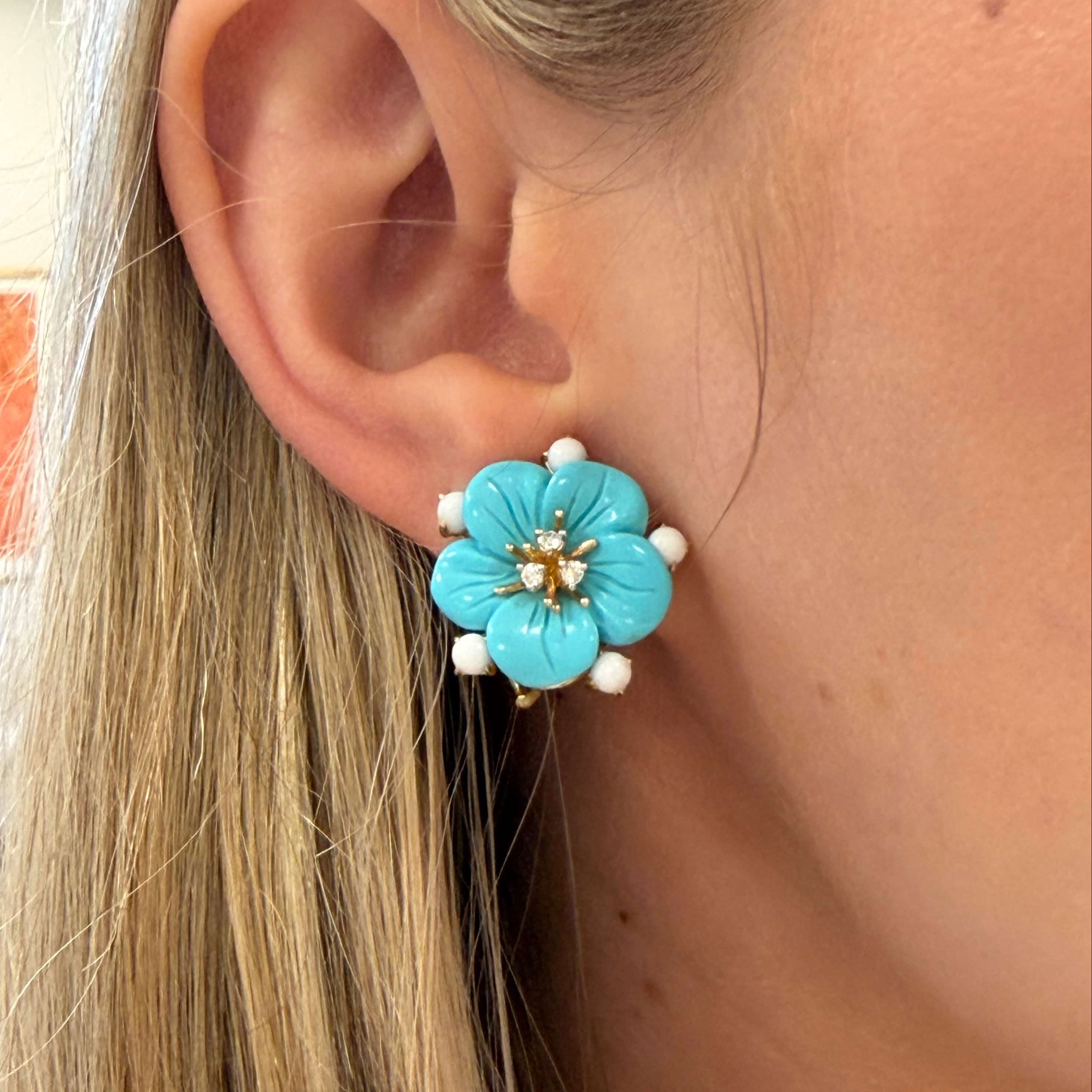 Close-up of a turquoise flower-shaped earring worn by a person with blonde hair.