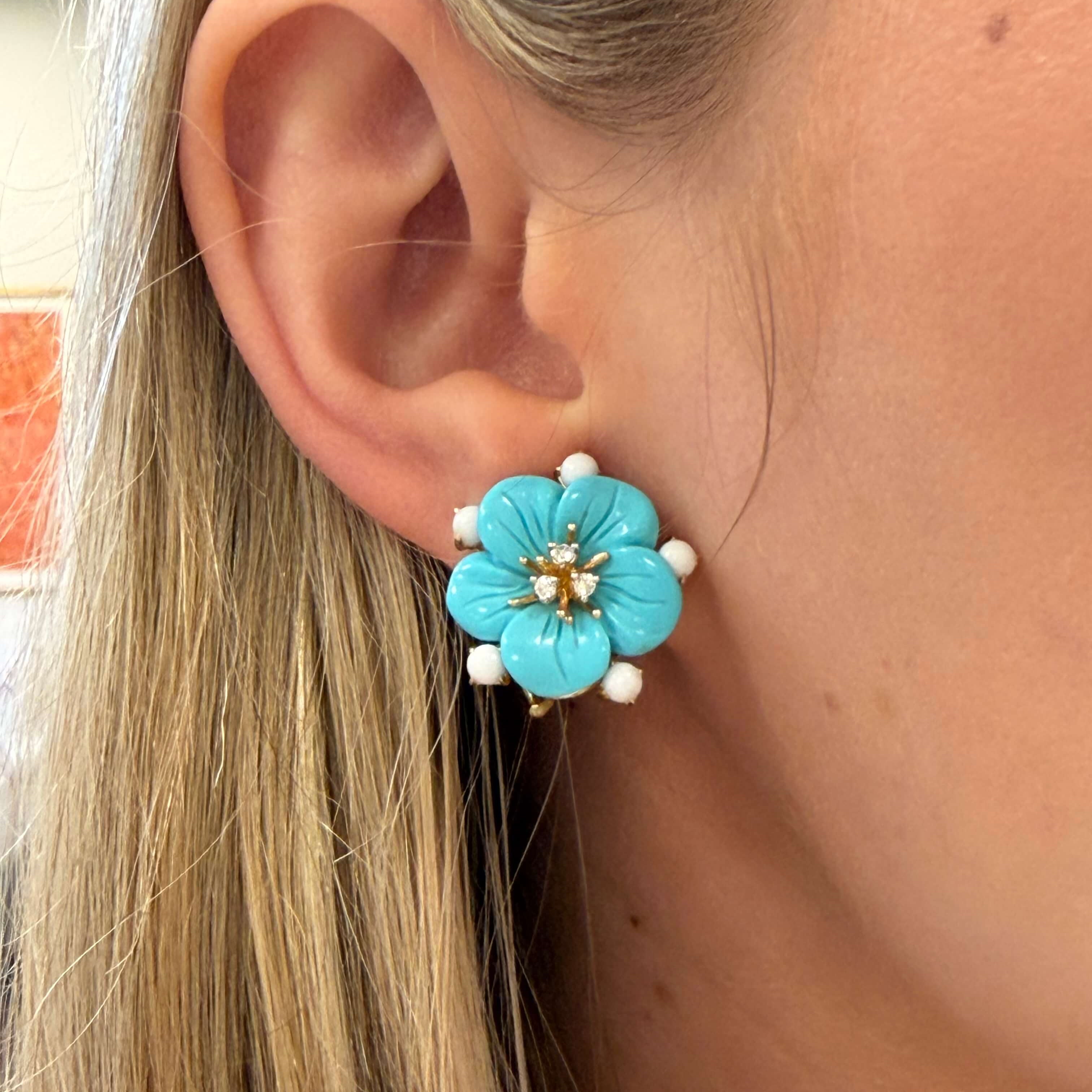Close-up of a turquoise flower-shaped earring worn by a person with blonde hair.