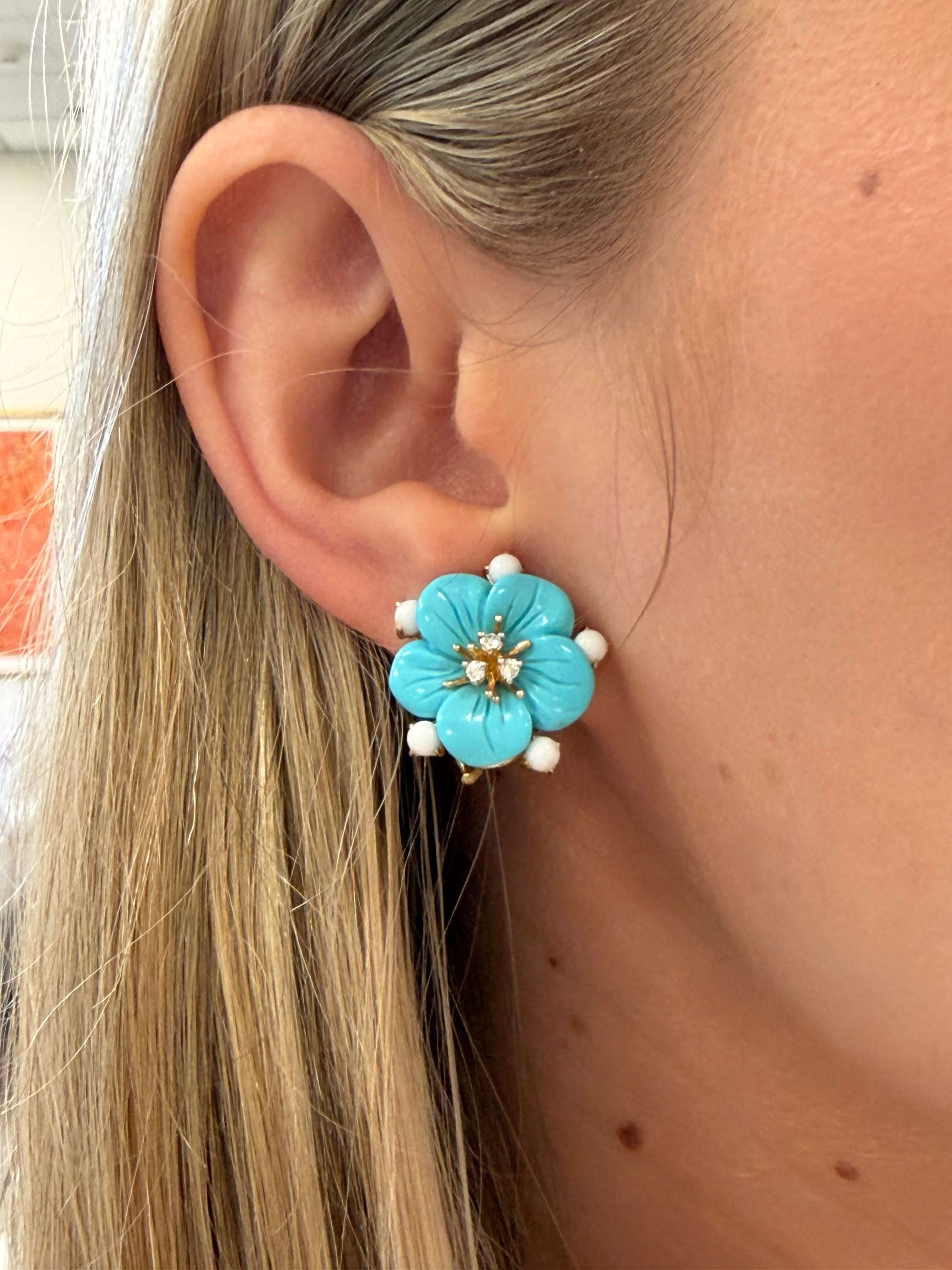 Close-up of a turquoise flower-shaped earring worn by a person with blonde hair.