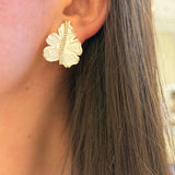 Close-up of a person wearing gold leaf-shaped earrings.