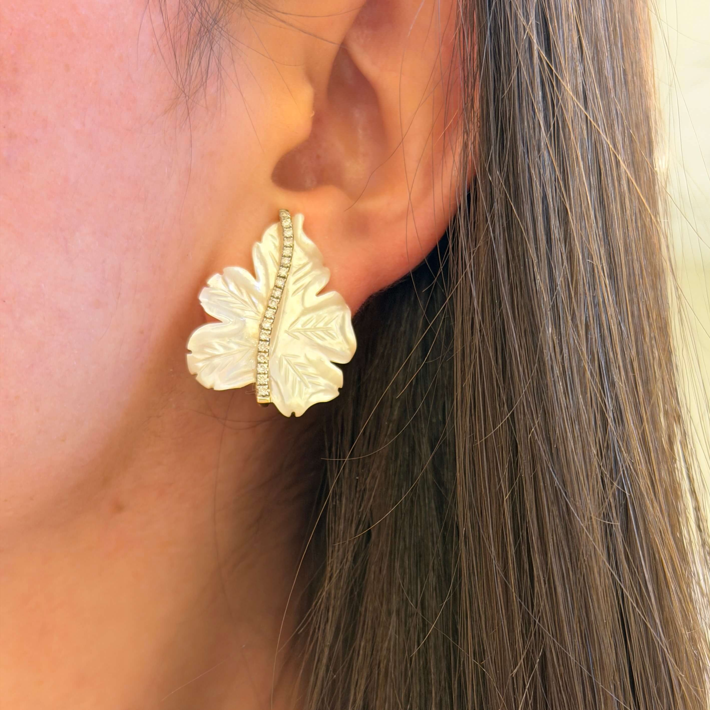 Close-up of a woman wearing 18K gold leaf-shaped earringswith diamonds
