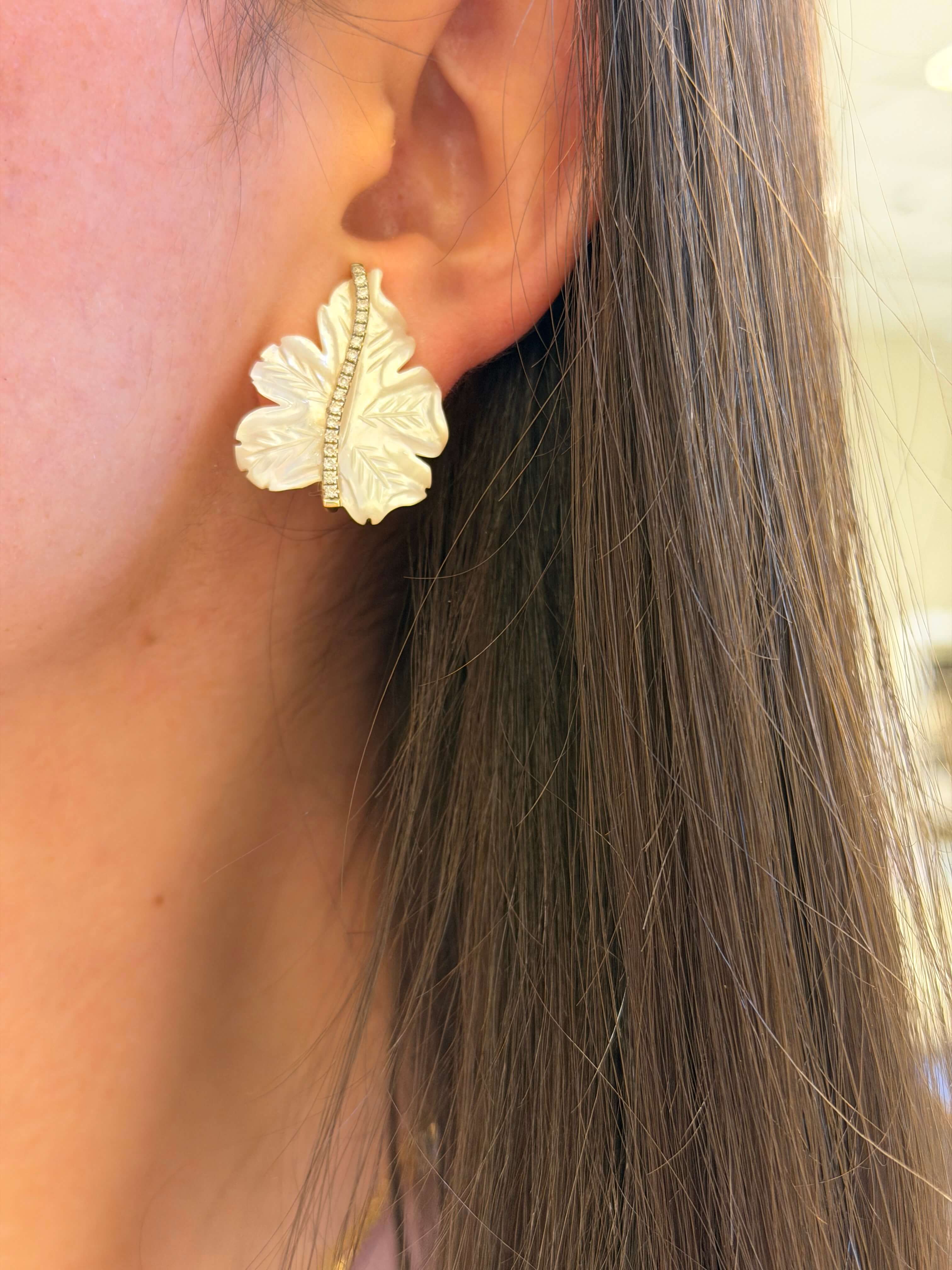 Close-up of a person wearing gold leaf-shaped earrings.