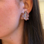 Close-up of an ear wearing a leaf-shaped earring with a blurred background