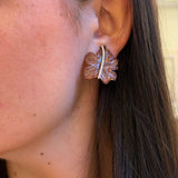 Close-up of an ear wearing a leaf-shaped earring with a blurred background